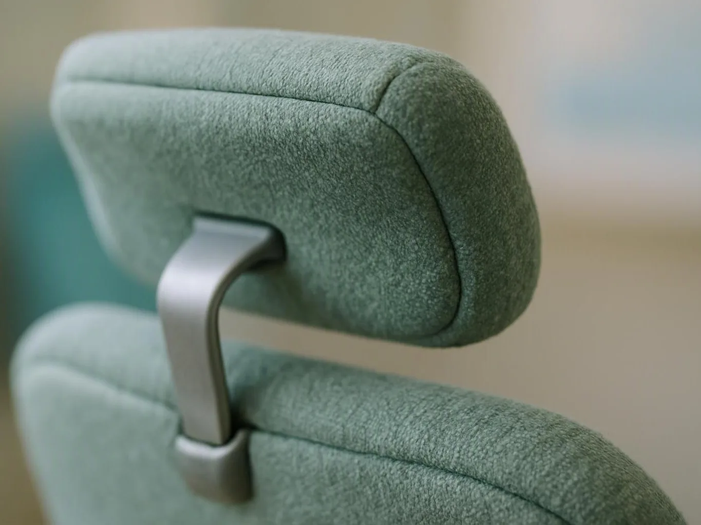 Close-up of a green upholstered chair headrest with a silver metal support against a blurred background